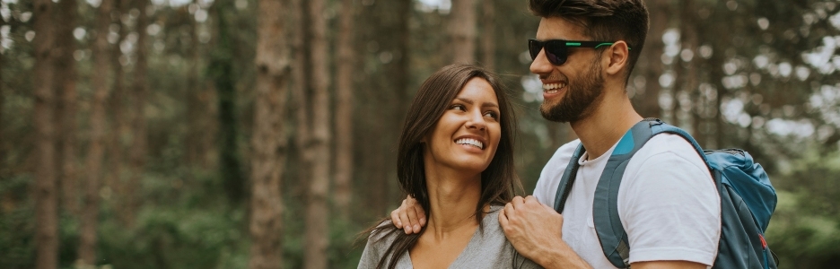 Imagen de pareja joven sonriente caminando con mochilas en el bosque en un día de verano