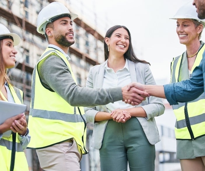 Imagen de cuando nos esforzamos por ser mejores de lo que somos. Toma de un equipo de constructores dándose la mano en un sitio de construcción afuera.